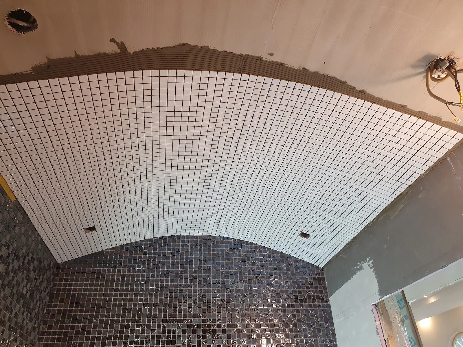 Gewölbte Decke im Verlegeprozess mit weißem und dunklem Mosaik im Übergang