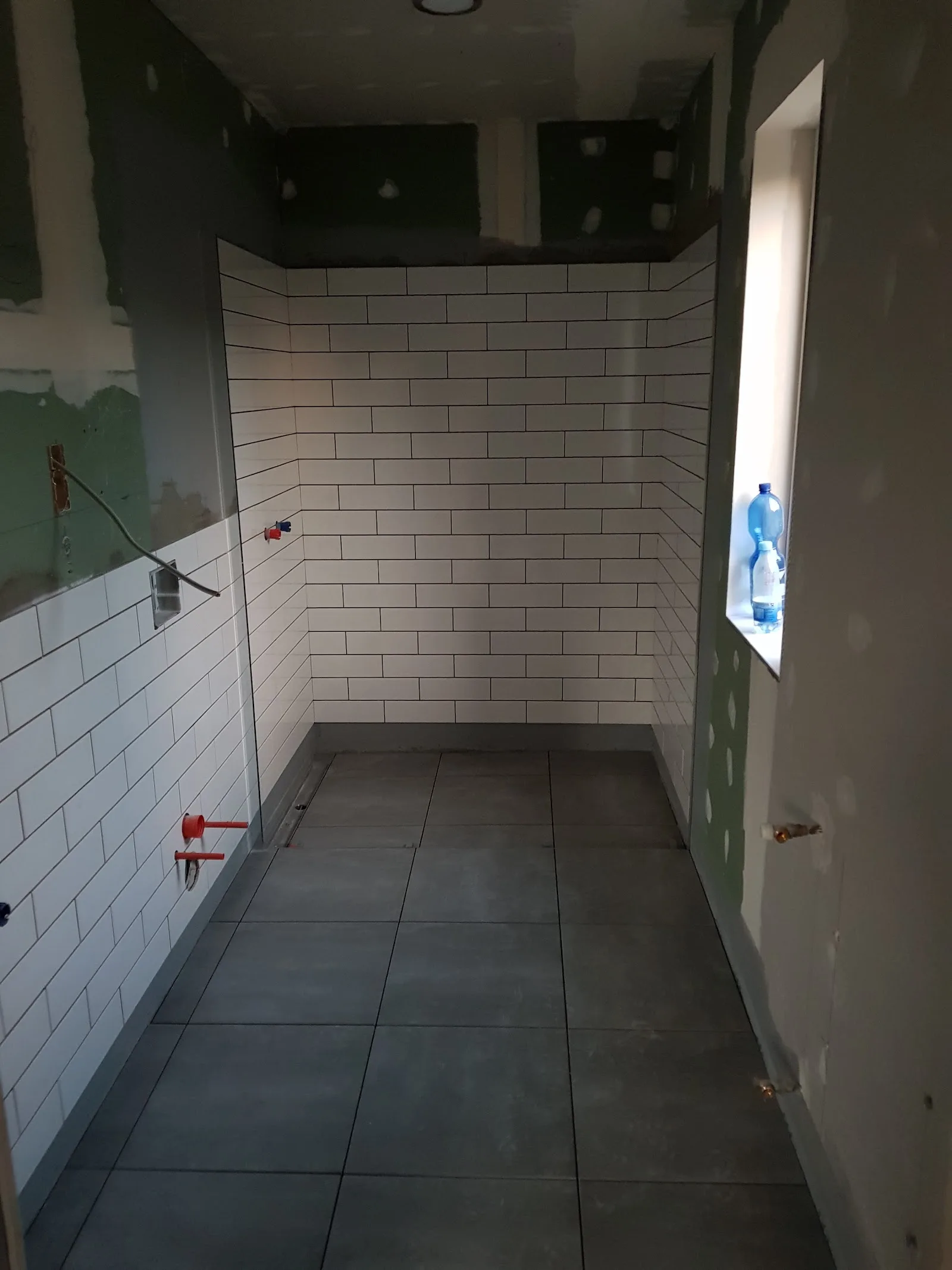 Fertige Dusche mit weißen Wandfliesen im Versatz und dunklem Boden