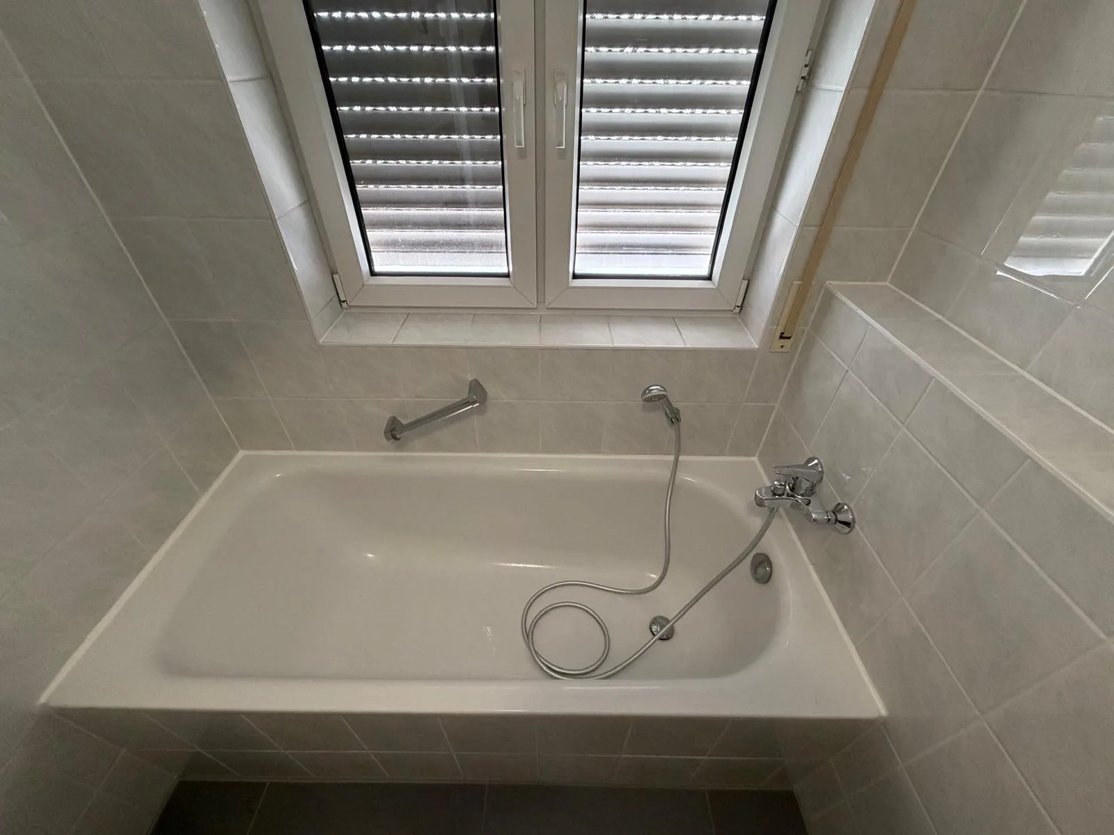 Fertiges Bad mit Badewanne unter dem Fenster und hellen Fliesen