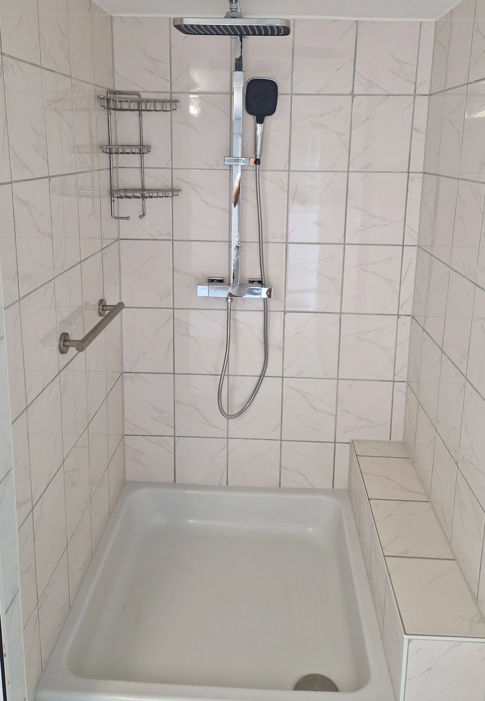 Fertige Dusche mit Kopfbrause, hellen Fliesen und gefliestem Podest an der rechten Wand